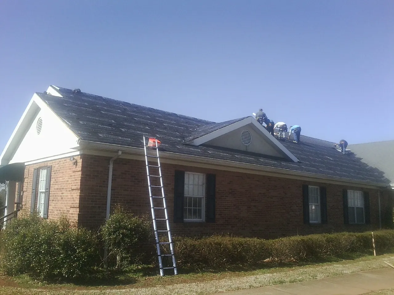 Crew tearing shingles off a brick ranch roof with a ladder set — Metal Roof Repair work by our crew in Dallastown