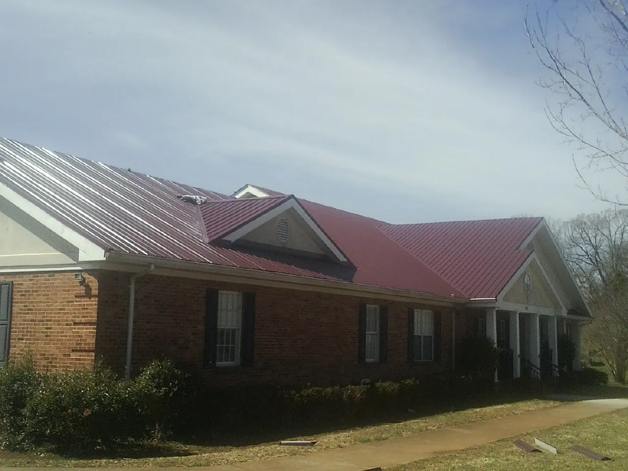 Red metal roof with gabled entries on a long brick building, from a Hail Damage Roof Repair job in Dallastown