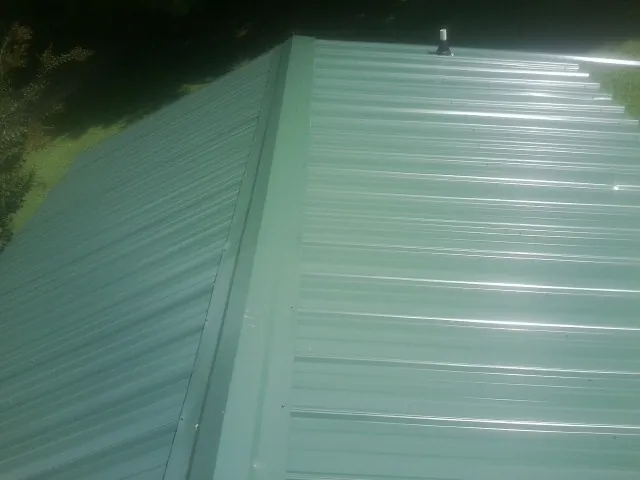 New green metal panels meeting at the ridge of a roof — Flat Roof Repair work by our crew in Dallastown