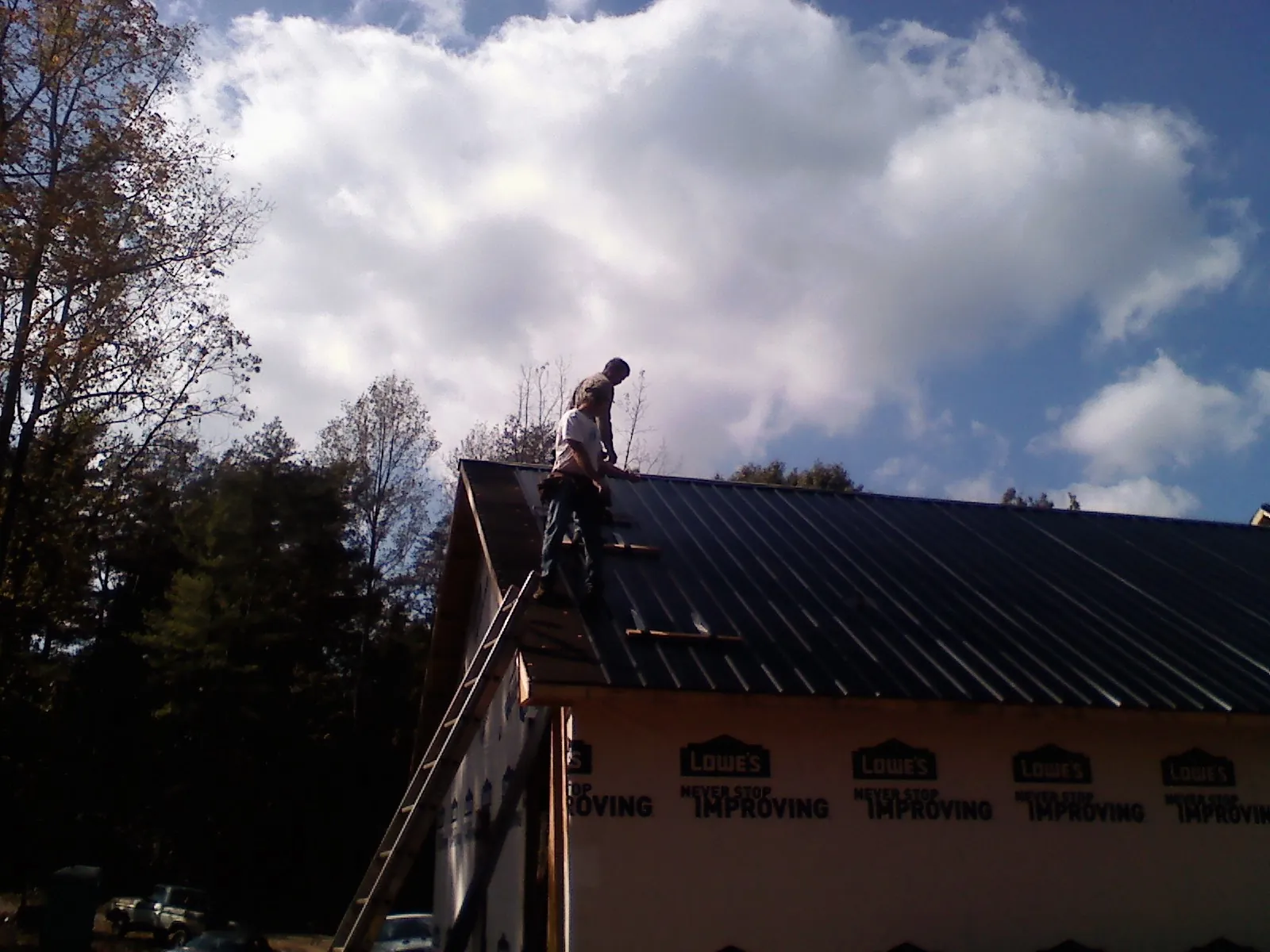 Roofer fastening dark metal panels high against a cloudy sky, from a Roof Inspection job in Dallastown