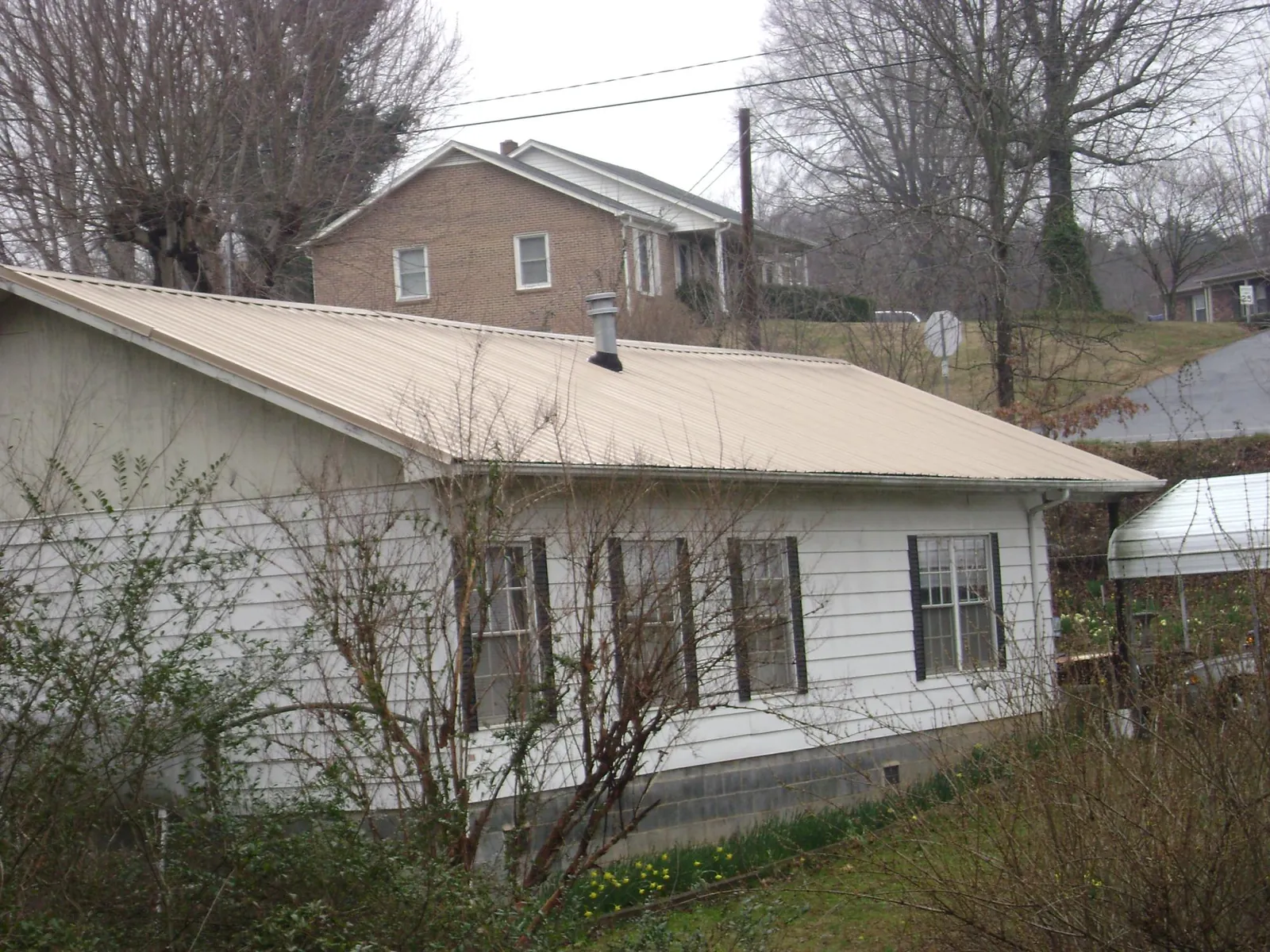 Tan metal roof on a white sided house set into a hillside — Commercial Roofing by Roofing Brothers in Dallastown